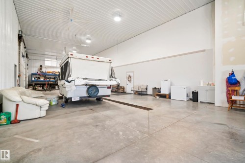Expansive concrete flooring with a central drainage system, high ceilings with exposed metal decking, and multiple ceiling-mounted fans - 49279 Rge Rd 240, Rural Leduc County, AB 