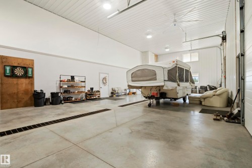 Spacious concrete floor with integrated drainage, white panel walls, and a large ceiling fan - 49279 Rge Rd 240, Rural Leduc County, AB 