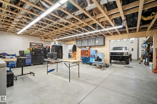 Expansive concrete flooring with exposed wood joist ceiling, featuring integrated overhead lighting and a wide garage door entry - 49279 Rge Rd 240, Rural Leduc County, AB 
