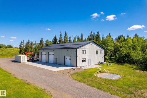 Two-story metal building featuring multiple roll-up doors, a flat roof, and a gravel driveway and home - 49279 Rge Rd 240, Rural Leduc County, AB 