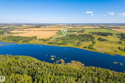 Expansive natural setting featuring a prominent body of water, surrounding wooded areas, and open fields under a clear sky - 49279 Rge Rd 240, Rural Leduc County, AB 