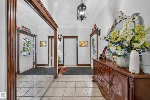White paneled entry door with sidelight, tile flooring, mirrored closet doors, and crown molding - 719 65 Ave Nw, Edmonton, AB 