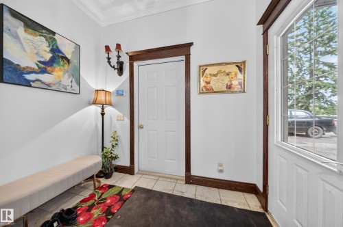 Foyer featuring crown molding, dark wood-finish trim, white paneled door, and tiled flooring - 719 65 Ave Nw, Edmonton, AB 