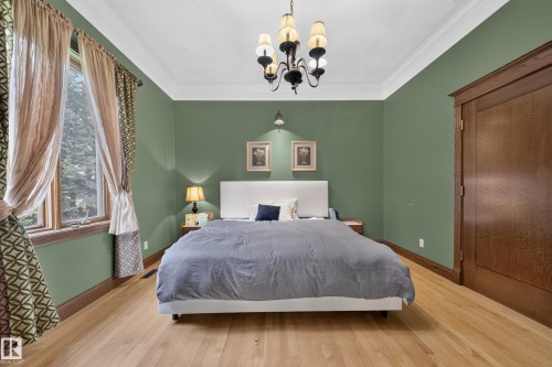 Hardwood flooring with a natural finish, crown molding, wall-mounted sconces, and a window with a wood frame - 719 65 Ave Nw, Edmonton, AB 