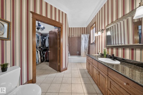 Ceramic tile flooring, built-in bathtub with tiled surround, wood-finish vanity with countertop, and an attached walk-in closet - 719 65 Ave Nw, Edmonton, AB 