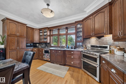 Wood-finish cabinetry with display elements, stainless steel double oven, stone countertops, integrated sink, and hardwood flooring - 719 65 Ave Nw, Edmonton, AB 