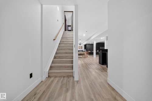 Light wood-finish flooring extending into the lower level, a staircase with wood treads, a wood handrail, and white risers - 719 65 Ave Nw, Edmonton, AB 