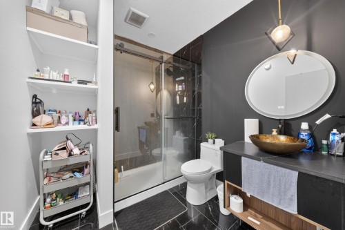 Modern bathroom featuring a glass-enclosed shower with black marble-look tiling, a round vessel sink, and a built-in vanity with open shelving - 719 65 Ave Nw, Edmonton, AB 