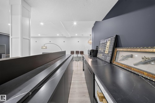 Dark cabinetry with integrated handles and a light-veined countertop, recessed ceiling lighting, light wood-finish flooring, and a dark accent wall - 719 65 Ave Nw, Edmonton, AB 