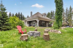 Expansive grassy area with a stone retaining wall, mature trees, and a fire pit - 