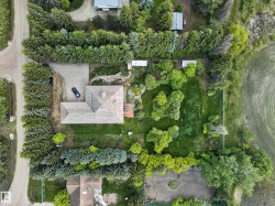 L-shaped roofline, paved driveway, surrounding mature evergreen trees, garden beds, and expansive green space - 