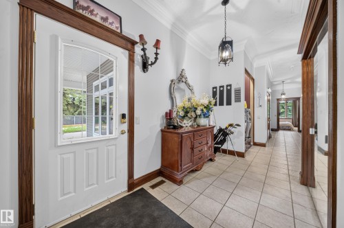 White paneled entry door with an arched window, dark wood-finish trim, tiled flooring, and crown molding - 719 65 Ave Nw, Edmonton, AB 