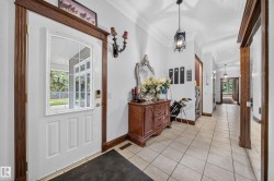 White paneled entry door with an arched window, dark wood-finish trim, tiled flooring, and crown molding - 