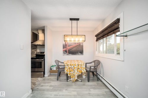 Wood-finish flooring, contemporary chandelier, bright window with blinds, and glass shelving - #202 10615 156 St Nw, Edmonton, AB 