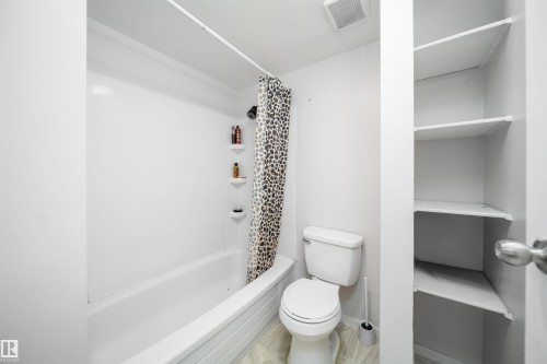 White bathtub with integrated shower, white toilet, and built-in shelving - #202 10615 156 St Nw, Edmonton, AB 