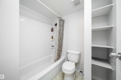 White bathtub with integrated shower, white toilet, and built-in shelving - 