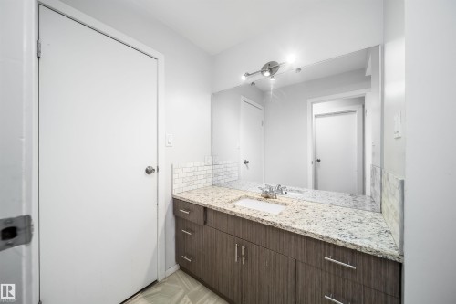 Vanity with wood-finish cabinetry, granite-style countertop, and subway tile backsplash - #202 10615 156 St Nw, Edmonton, AB 