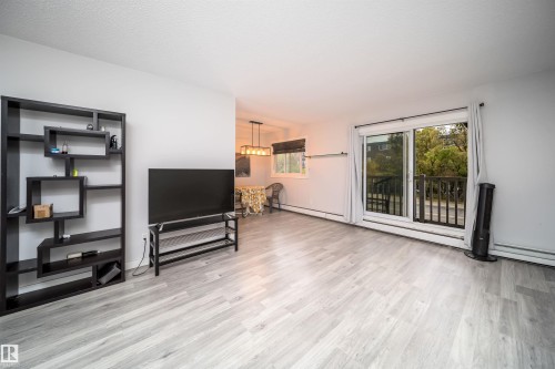 Light grey wood-finish flooring, white walls, and a sliding glass door leading to an exterior balcony with dark railings - #202 10615 156 St Nw, Edmonton, AB 