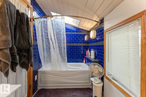 Bathtub with blue tiled surround, built-in shelving, wood-paneled ceiling, and a window with blinds - #421 61209 Rge Rd 465, Rural Bonnyville M.D., AB 