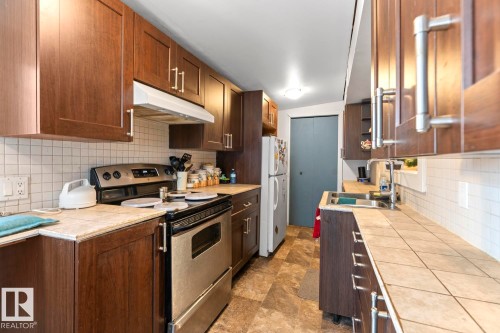 Kitchen featuring extensive wood-finish cabinetry, stainless steel appliances, tiled countertops, a white subway tile backsplash, and resilient flooring - #421 61209 Rge Rd 465, Rural Bonnyville M.D., AB 