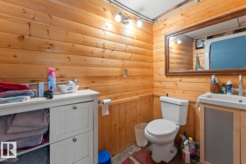 Wood paneling throughout, a wall-mounted mirror, white toilet, and a white vanity with an integrated sink - #421 61209 Rge Rd 465, Rural Bonnyville M.D., AB 