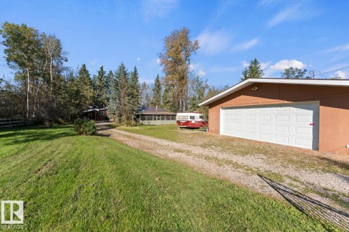 Detached garage with two white panel doors, gravel driveway, and surrounding green space with mature trees - #421 61209 Rge Rd 465, Rural Bonnyville M.D., AB 