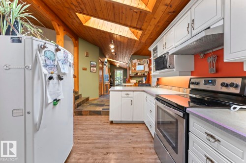 Vaulted wood-paneled ceiling with skylights, white cabinetry, stainless steel appliances, and wood-finish flooring - #421 61209 Rge Rd 465, Rural Bonnyville M.D., AB 