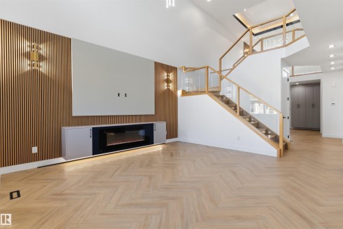 Herringbone wood-finish flooring, built-in electric fireplace, slatted wood accent wall, contemporary staircase with glass railing, and integrated wall sconces - 2720 63 Avenue, Rural Leduc County, AB 