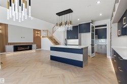 Herringbone wood-finish flooring, two-tone kitchen island with a built-in sink, dark blue cabinetry with gold-tone hardware, contemporary linear fireplace, and a wood-slat accent wall - 