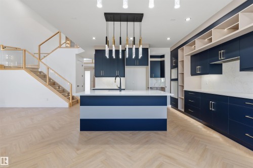 Modern kitchen with a multi-tone island, pendant lighting, built-in cabinetry, and wood-finish flooring - 2720 63 Avenue, Rural Leduc County, AB 