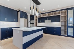 Kitchen featuring navy cabinetry, white countertops, a central island with an integrated sink, herringbone wood-finish flooring, and a linear pendant light fixture - 