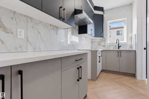 Kitchen featuring light wood-finish herringbone flooring, black upper cabinetry, light gray lower cabinetry, and white countertops with a matching backsplash - 2720 63 Avenue, Rural Leduc County, AB 