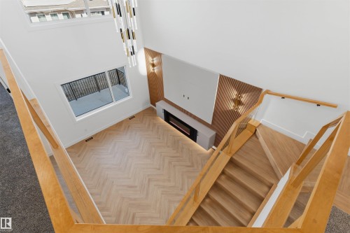 Two-story ceiling, wood-finish flooring with a herringbone pattern, contemporary chandelier, built-in electric fireplace, and light wood staircase with glass panels - 2720 63 Avenue, Rural Leduc County, AB 