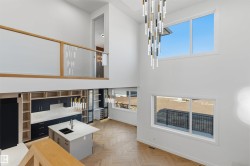 Two-story living area with high ceilings, large windows, wood-finish flooring, and a contemporary linear chandelier - 