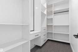 Custom white cabinetry with multiple shelving units, built-in drawers, hanging rods, and a dressing area - 