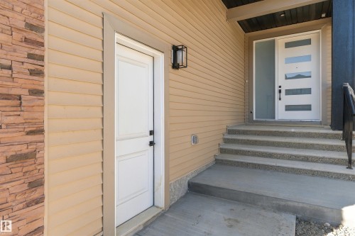 Modern entry with a multi-paneled front door and frosted sidelight, featuring a concrete staircase with textured risers, and a stone veneer accent wall - 2720 63 Avenue, Rural Leduc County, AB 