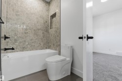 Bathtub with floor-to-ceiling marbled tile surround, featuring a recessed niche and matte black fixtures - 