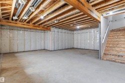 Unfinished basement featuring exposed wood joists, concrete flooring, and insulated perimeter walls - 