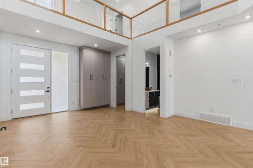 Herringbone wood-finish flooring, custom built-in cabinetry, modern entry door with frosted glass panels, recessed lighting, and a glass railing mezzanine - 2720 63 Avenue, Rural Leduc County, AB 