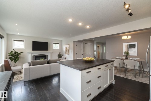Open-concept living space featuring wood-finish flooring, a white kitchen island with an integrated sink, a built-in fireplace with a mantel, recessed lighting, and a chandelier - 55 Michigan Street, Devon, AB 