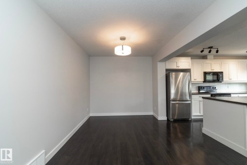 Open concept layout, dark wood-finish flooring, recessed lighting, white cabinetry, stainless steel refrigerator - 55 Michigan Street, Devon, AB 