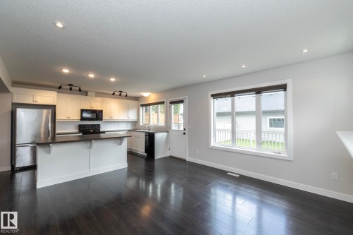 Open-concept living space with dark wood-finish flooring, recessed lighting, and a white kitchen featuring stainless steel appliances - 55 Michigan Street, Devon, AB 