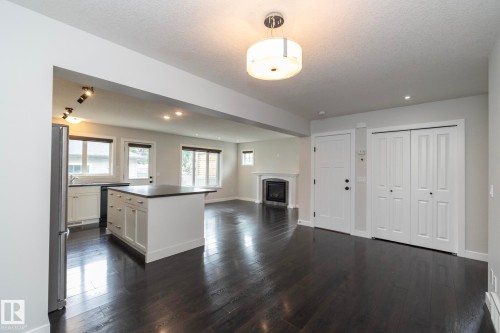 Dark wood-finish flooring, white kitchen cabinetry, a kitchen island with dark countertop, a built-in fireplace, and a ceiling-mounted light fixture - 55 Michigan Street, Devon, AB 