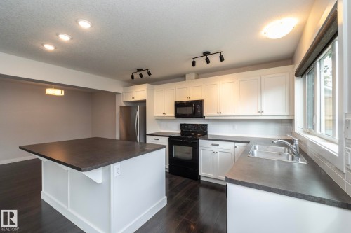 Bright kitchen featuring white cabinetry, dark countertops, dark wood-finish flooring, a stainless steel refrigerator, and a kitchen island - 55 Michigan Street, Devon, AB 