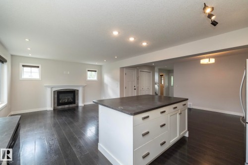 Expansive living area featuring dark wood-finish flooring, a central island with white cabinetry, recessed lighting, a fireplace with a white mantel, and a stainless steel refrigerator - 55 Michigan Street, Devon, AB 