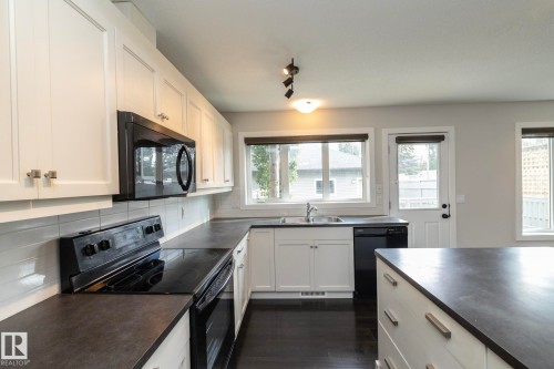 Contemporary kitchen featuring white cabinetry, black appliances, dark countertops, and wood-finish flooring - 55 Michigan Street, Devon, AB 