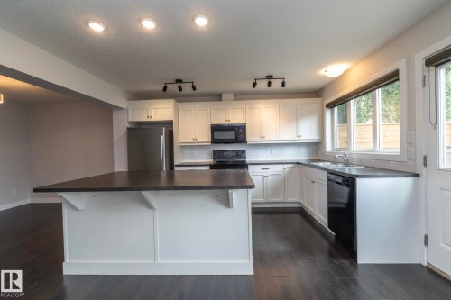 Kitchen featuring a central island, white cabinetry, dark countertops, and stainless steel appliances - 55 Michigan Street, Devon, AB 