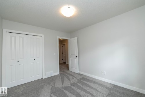 Light gray wall paint, patterned gray carpeting, white bi-fold closet doors, white interior door with black hardware, and a ceiling-mounted light fixture - 55 Michigan Street, Devon, AB 