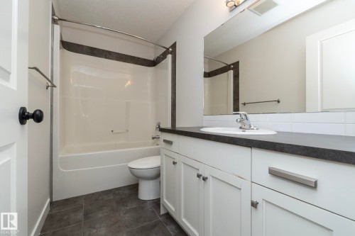 Bathroom featuring a white vanity with a dark countertop, an integrated sink, white subway tile backsplash, and dark tile flooring - 55 Michigan Street, Devon, AB 
