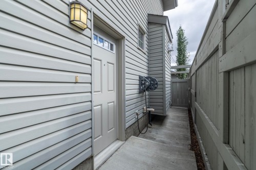Light-colored horizontal siding exterior with a paneled entry door featuring a transom window, a fixed outdoor wall sconce, and a concrete walkway - 55 Michigan Street, Devon, AB 